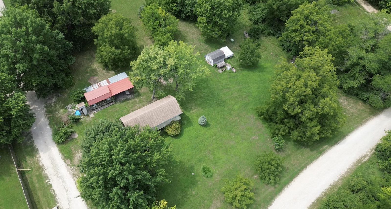 Aerial view of the 0.62-acre Lake Arrowhead lot, showing the covered RV structure, storage sheds, and tree line